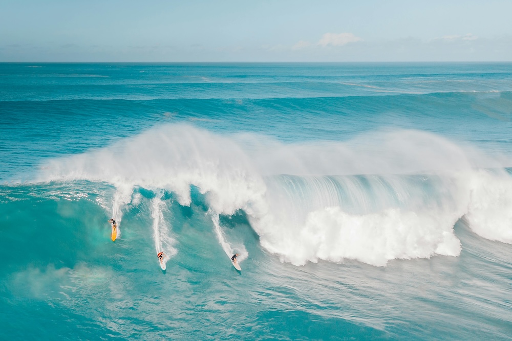 three surfers on a big wave in Hawaii