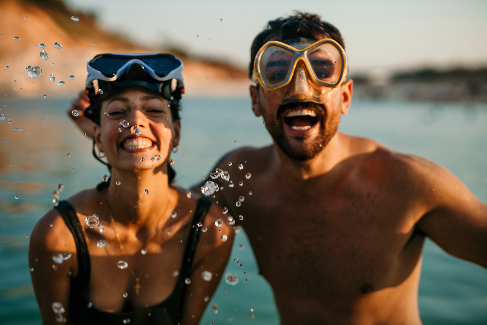 couple with snorkel goggles on face standing on beach